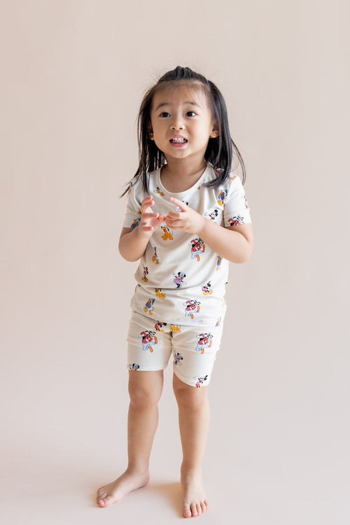 Girl wearing Short Sleeve Pajamas in Mickey Mouse & Friends print standing on a cream background