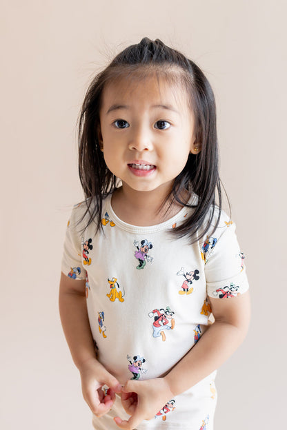 Girl wearing Short Sleeve Pajamas in Mickey Mouse & Friends print on a cream background