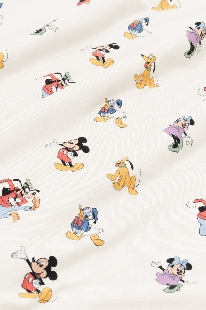Close up of bamboo fabric swatch: An all-over print featuring: Mickey Mouse in his classic red shorts with white buttons and yellow shoes; Minnie Mouse wearing a blue headbow, a pink dress, and green heels; Goofy jumping in the air and wearing a green hat, a red shirt, blue pants, and orange shoes; Pluto wearing a green collar; and Donald Duck in his classic blue sailor outfit and hat, over a warm grey background color called Oat.