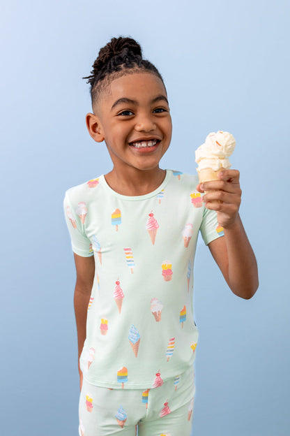 Child smiling with an ice cream cone wearing short sleeve pajama set in Mint Ice Cream print on a blue background