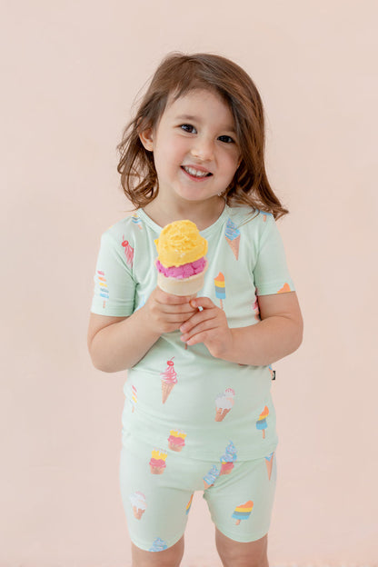 Child wearing short sleeve pajama set in Mint Ice Cream print smiling with an ice cream cone on a beige background