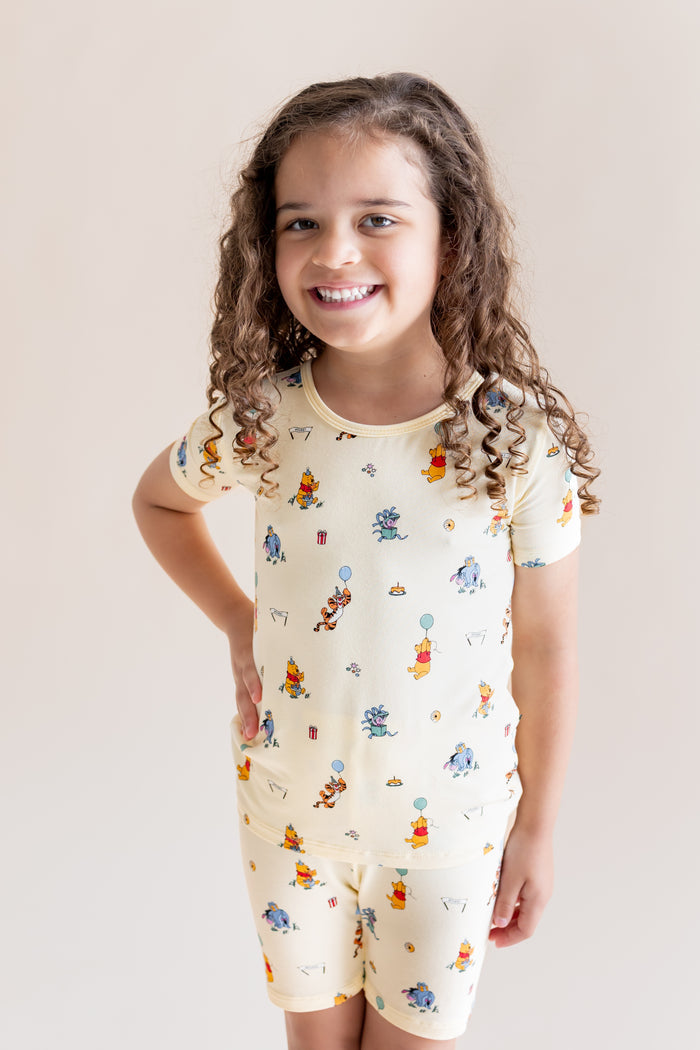 Girl smiling in Short Sleeve Pajamas in Winnie the Pooh Celebration print on a cream background