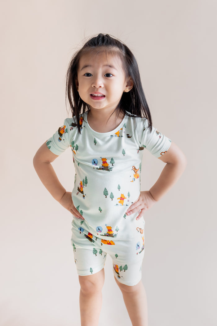 Girl posing in Short Sleeve Pajamas in Winnie the Pooh Hundred Acre Wood print on a cream background
