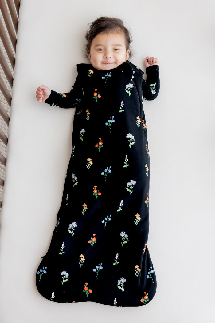 Baby lying in a crib wearing Sleep Bag in Midnight Wildflower 1.0 print over a white crib sheet