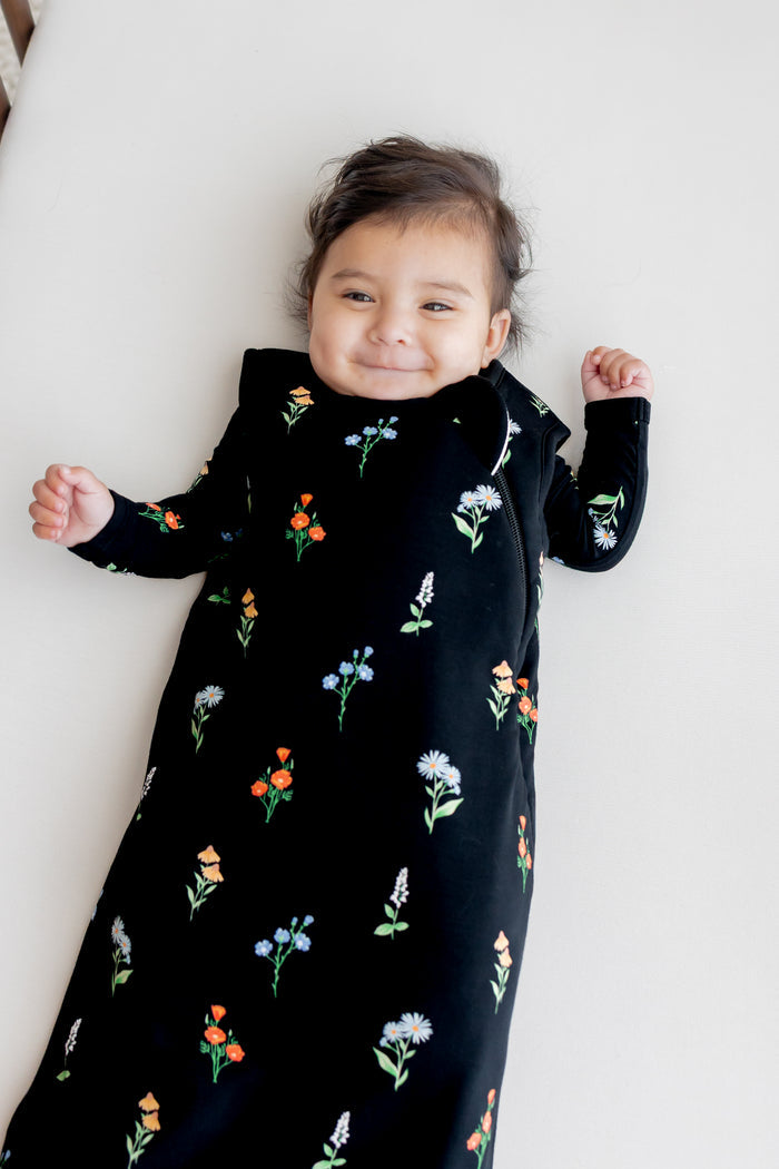 Baby smiling in a crib wearing Sleep Bag in Midnight Wildflower 1.0 print over a white crib sheet