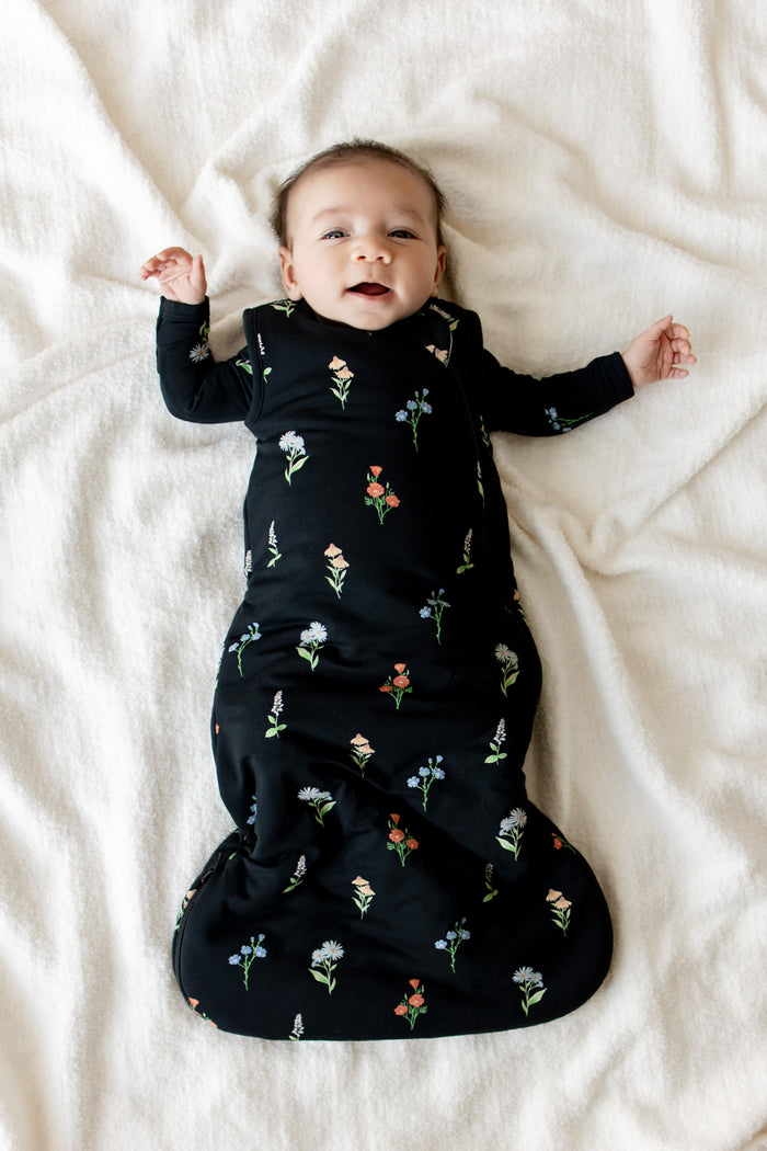 Baby lying on a white sheet wearing Sleep Bag in Midnight Wildflower 1.0 print