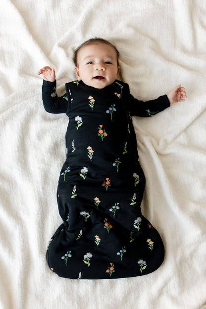 Baby lying on a white sheet wearing Sleep Bag in Midnight Wildflower 1.0 print