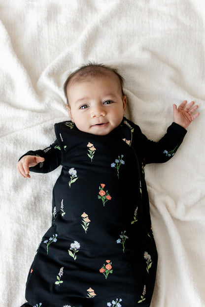 Baby wearing Sleep Bag in Midnight Wildflower 1.0 print lying over white sheet