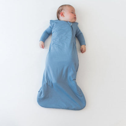 Baby sleeping on a flat off-white surface in the 2.5 Sleep Bag in Slate