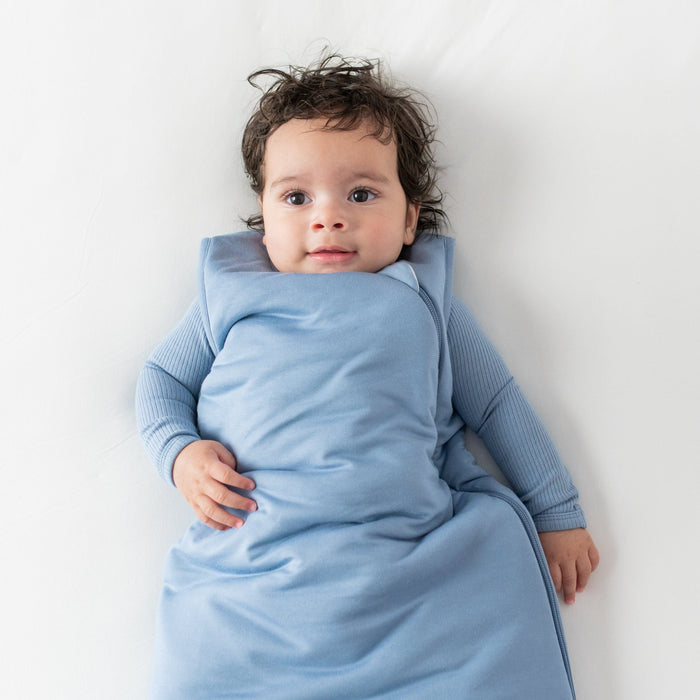 Baby laying on its back on an off white surface and wearing a Sleep Bag in Slate in 2.5 TOG