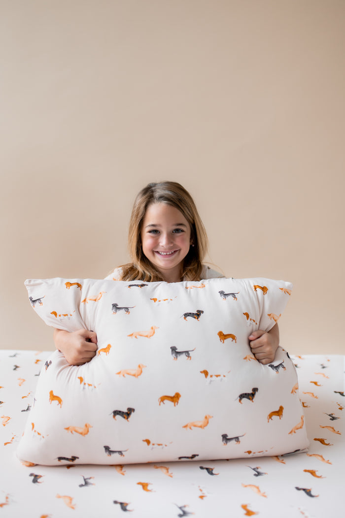 Girl holding Standard Pillowcase in Dachshund print sitting on a similar print sheet