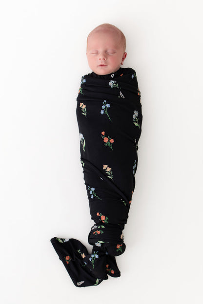 Baby swaddled in Swaddle Blanket in Midnight Wildflower print on a white background