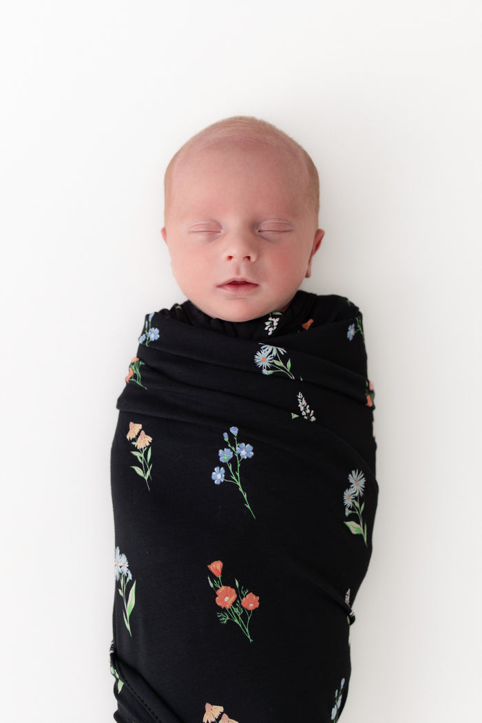Baby sleeping in Swaddle Blanket in Midnight Wildflower print on a white background