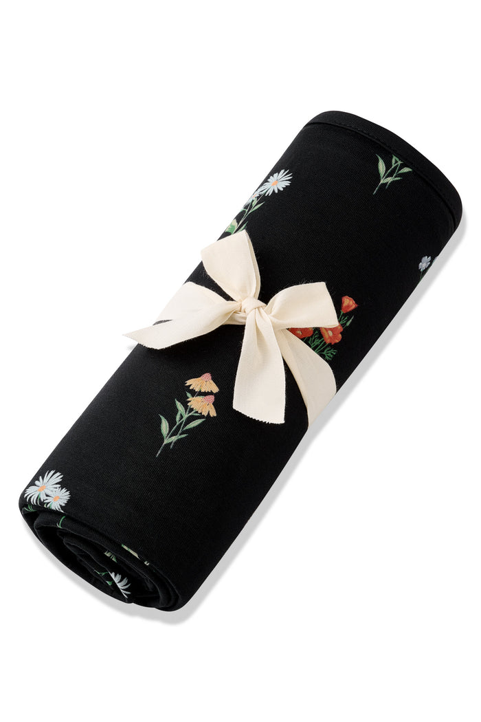 Black Swaddle Blanket in Wildflower print rolled in a ribbon on a white background