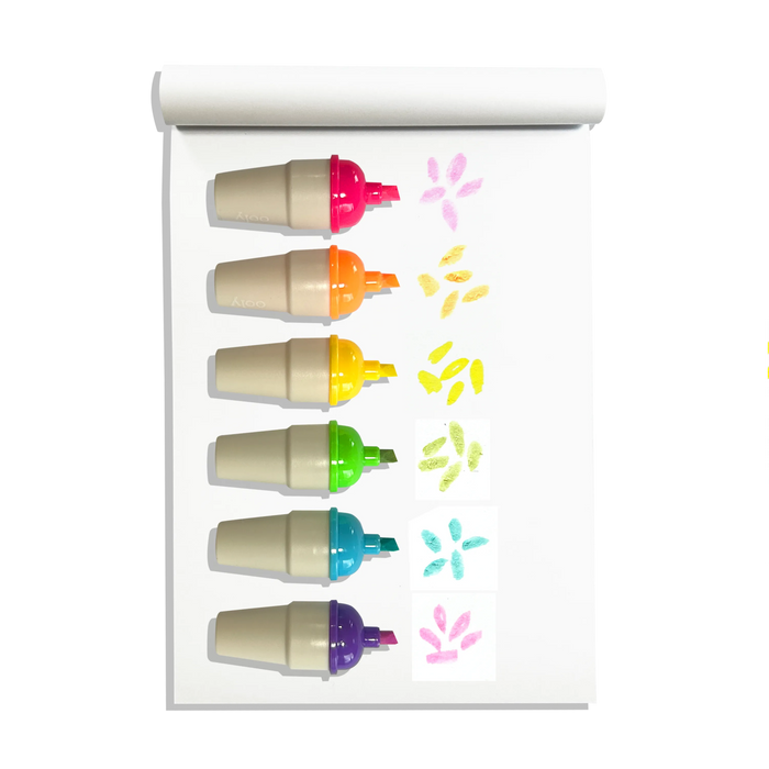 Row of uncapped OOLY Sweet Scoops Scented Neon Highlighters on a white sketchbook with colored swatches