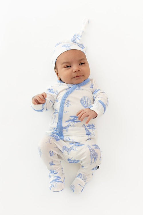 Newborn laying on a white surface wearing the Take Me Home Set with Cap in Toile Safari