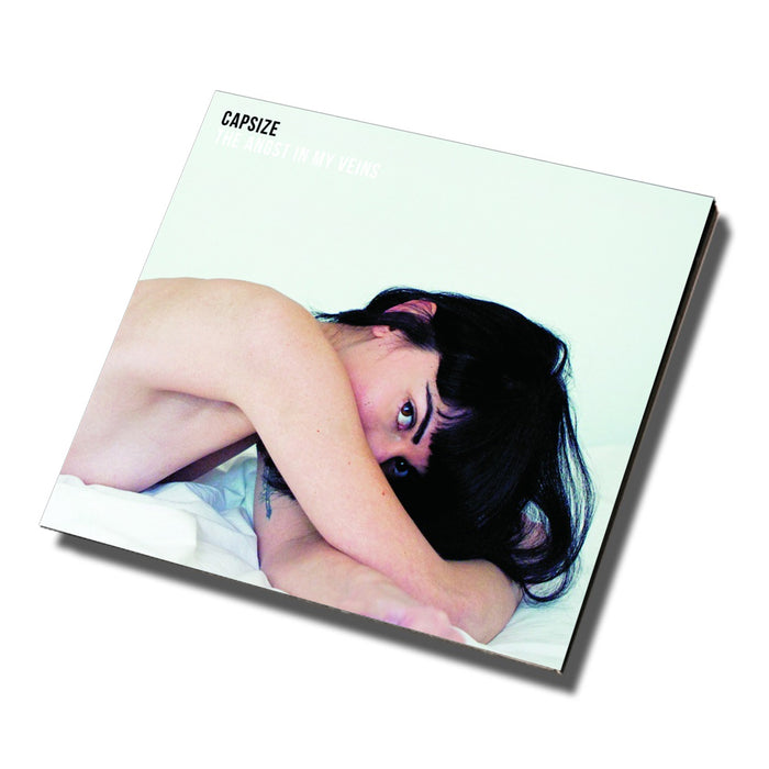Album cover for Capsize CD Angst In My Veins, showing a person with dark hair lying in bed, gazing at the camera against a soft white background, with pale text and part of the track list in the upper left.