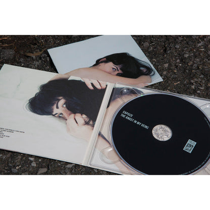 A CD case lies open on the ground, revealing a Capsize The Angst In My Veins CD and booklet featuring a woman with dark hair on a white surface, partially covering her face.