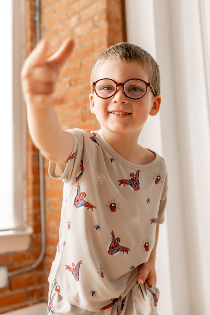 Boy in specs wearing oat color Toddler Basic Tee with Spider-Man print showing spider man finger gesture