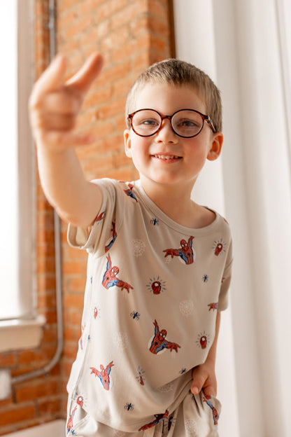Boy in specs wearing oat color Toddler Basic Tee with Spider-Man print showing spider man finger gesture