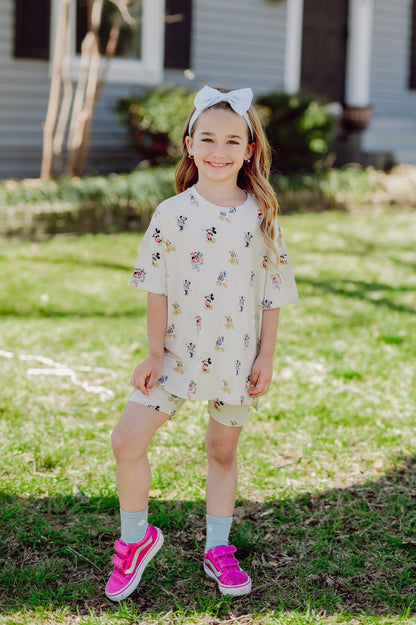 Young girl in a mickey and friends matching biker set and hot pink sneakers in front of a house