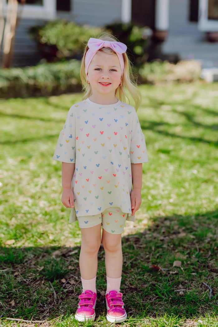 Young girl in a biker set with a colorful mickey mouse head pattern and hot pink sneakers outdoors