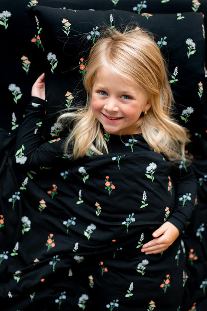 Girl lying on Toddler Pillowcase in Midnight Wildflower print covered under similar print Toddler blanket and sheets