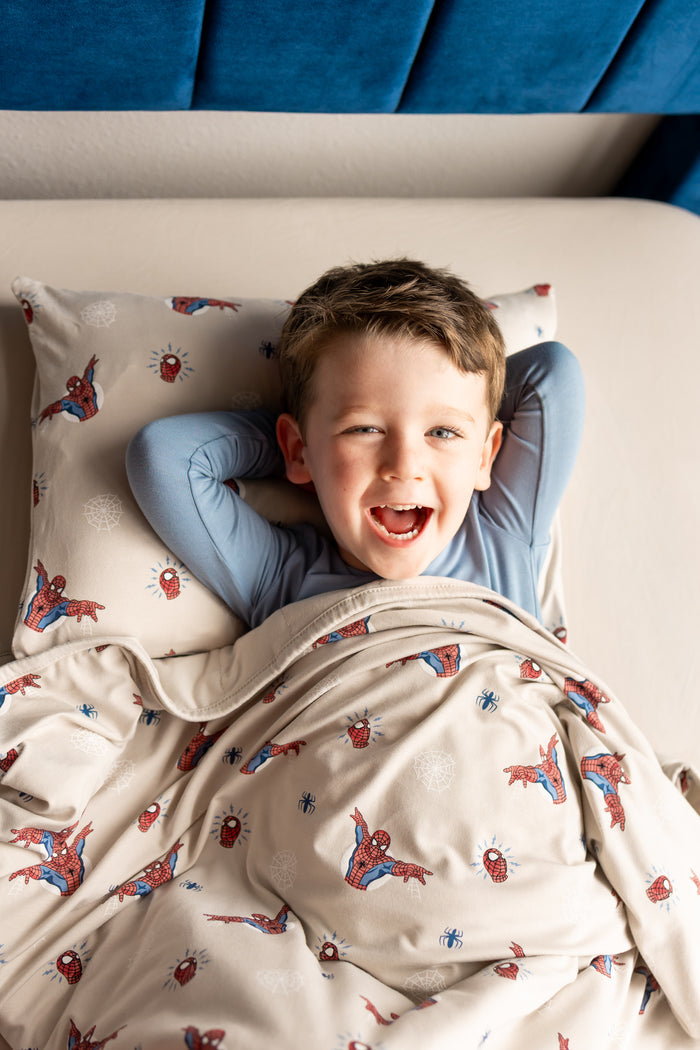 Boy lying on a bed under an oat color Toddler Blanket with Spider-Man print over similar print pillowcase