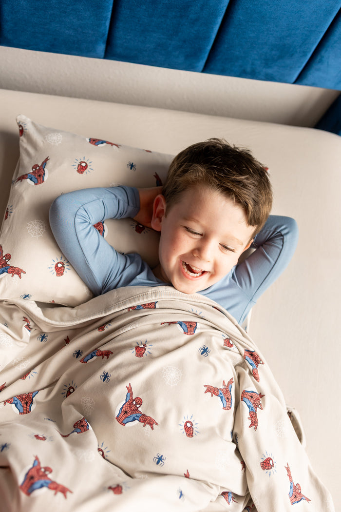 Boy lying on bed over oat color sheets and Spider-Man print pillowcase covered under oat color Toddler Blanket with Spider-Man print