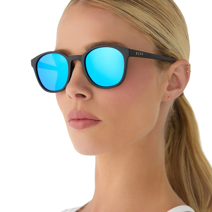 on model - female wearing diff sport featuring the volley round sunglasses with a matte black frame and blue mirror polarized lenses angled view