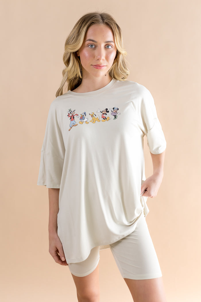 Woman wearing a white oversized t-shirt with cartoon character design and biker shorts on a beige background