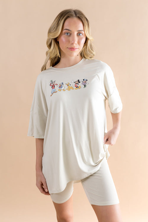 Woman wearing a white oversized t-shirt with cartoon character design and biker shorts on a beige background