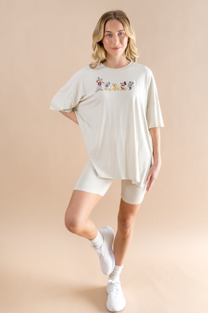 Woman wearing biker short set featuring an oversized tee with mickey cartoon print and wearing white socks and sneakers