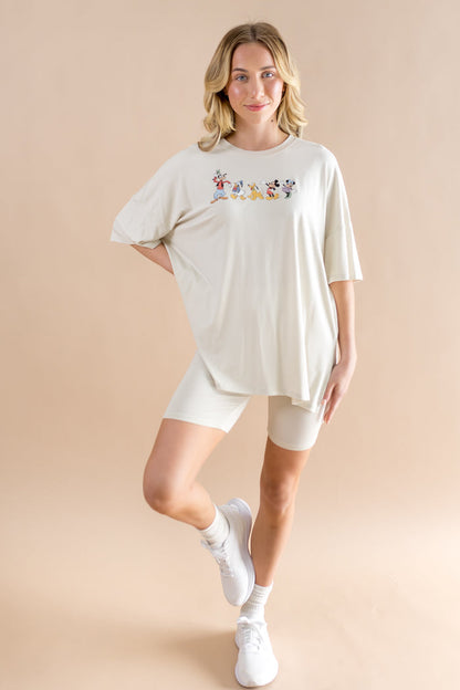 Woman wearing biker short set featuring an oversized tee with mickey cartoon print and wearing white socks and sneakers