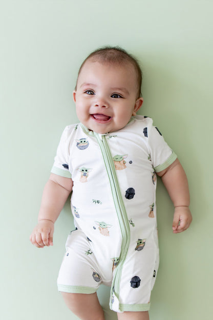 Close up of infant wearing the Zipper Shortall Romper in Grogu™ on a light green surface