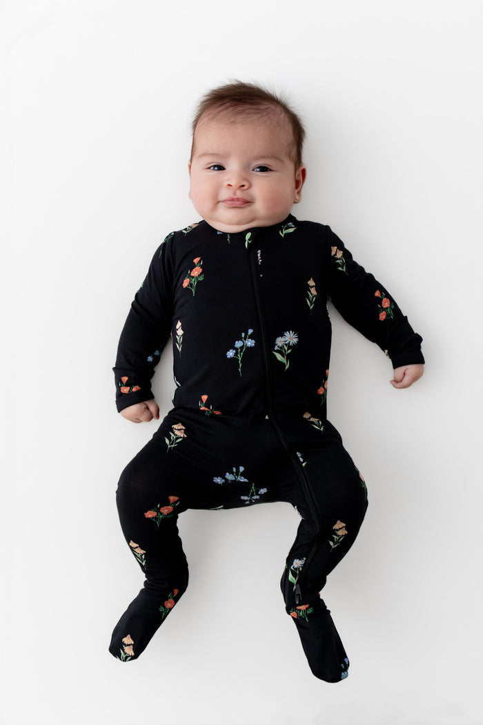 Baby wearing Zippered Footie in Midnight Wildflower print on a white background