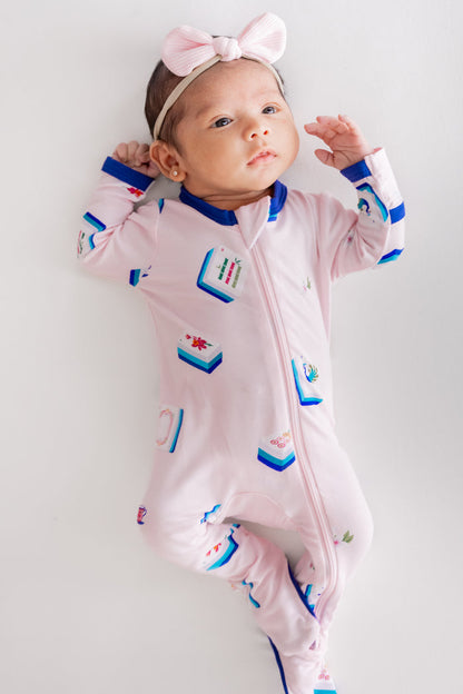 Baby wearing Zippered Footie in Sakura Mahjong print and pink bow headband lying on a beige background