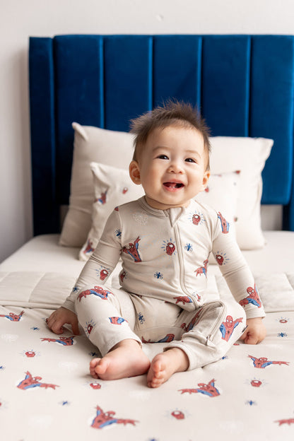 Baby sitting on bed wearing oat color Zippered Romper with Spider-Man print