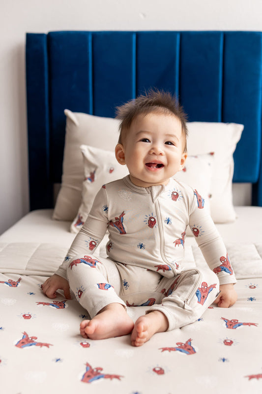 Baby sitting on bed wearing oat color Zippered Romper with Spider-Man print