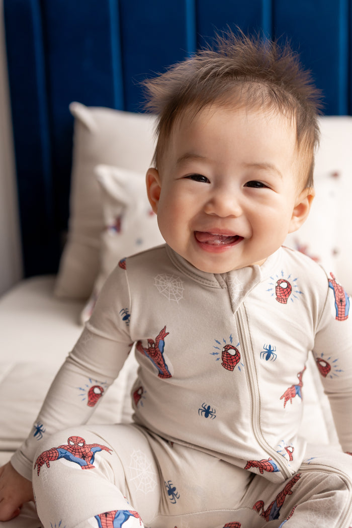 Baby smiling on bed wearing oat color Zippered Romper with Spider-Man print