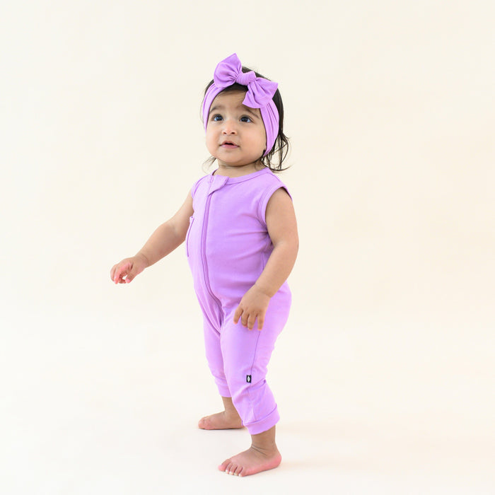 Toddler wearing Kyte Baby Sleeveless Zippered Romper in Poi with matching bow